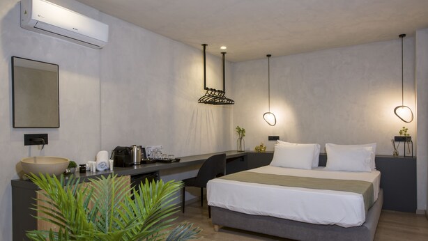 Ein modernes Hotelzimmer mit einem großen Bett, einem Schreibtisch, einem Stuhl, einem kleinen Tisch mit Pflanze und einer Klimaanlage.