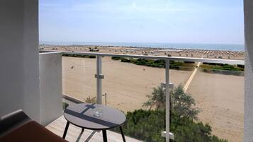 Balcón con mesa y silla con vista a una playa, un estacionamiento y un cielo despejado.