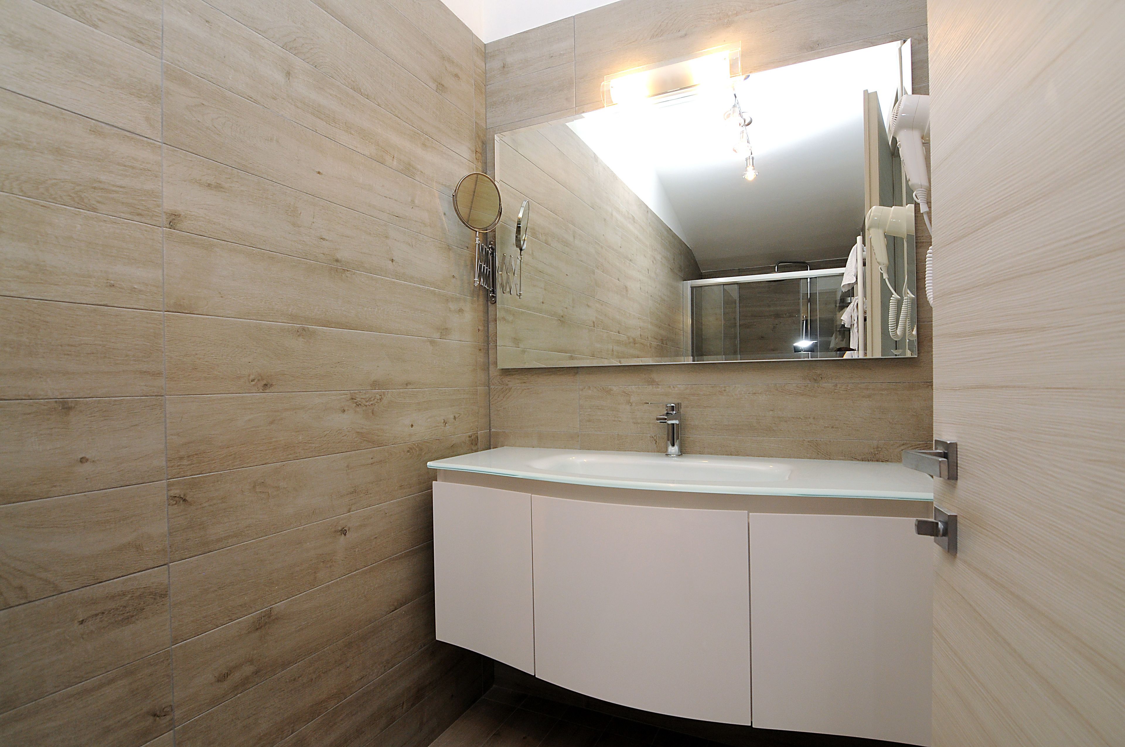 A modern bathroom with a wooden wall, a white sink, and a large mirror.
