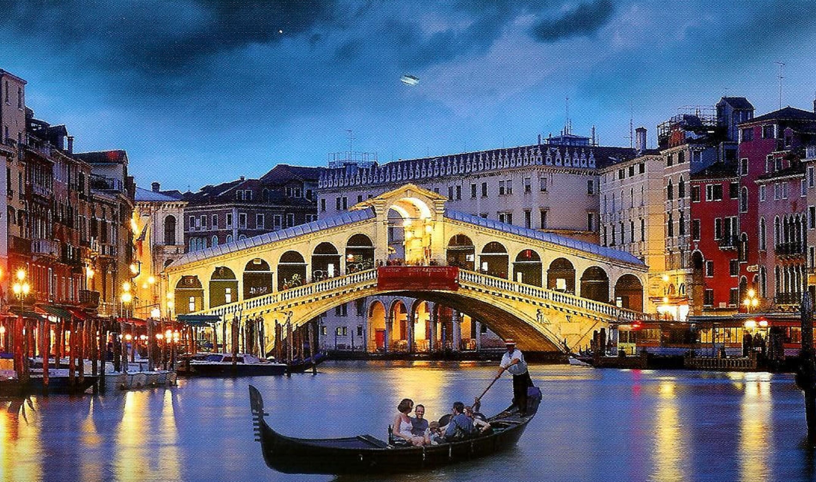 A historic bridge with a red arch over a canal, surrounded by buildings with illuminated windows.
