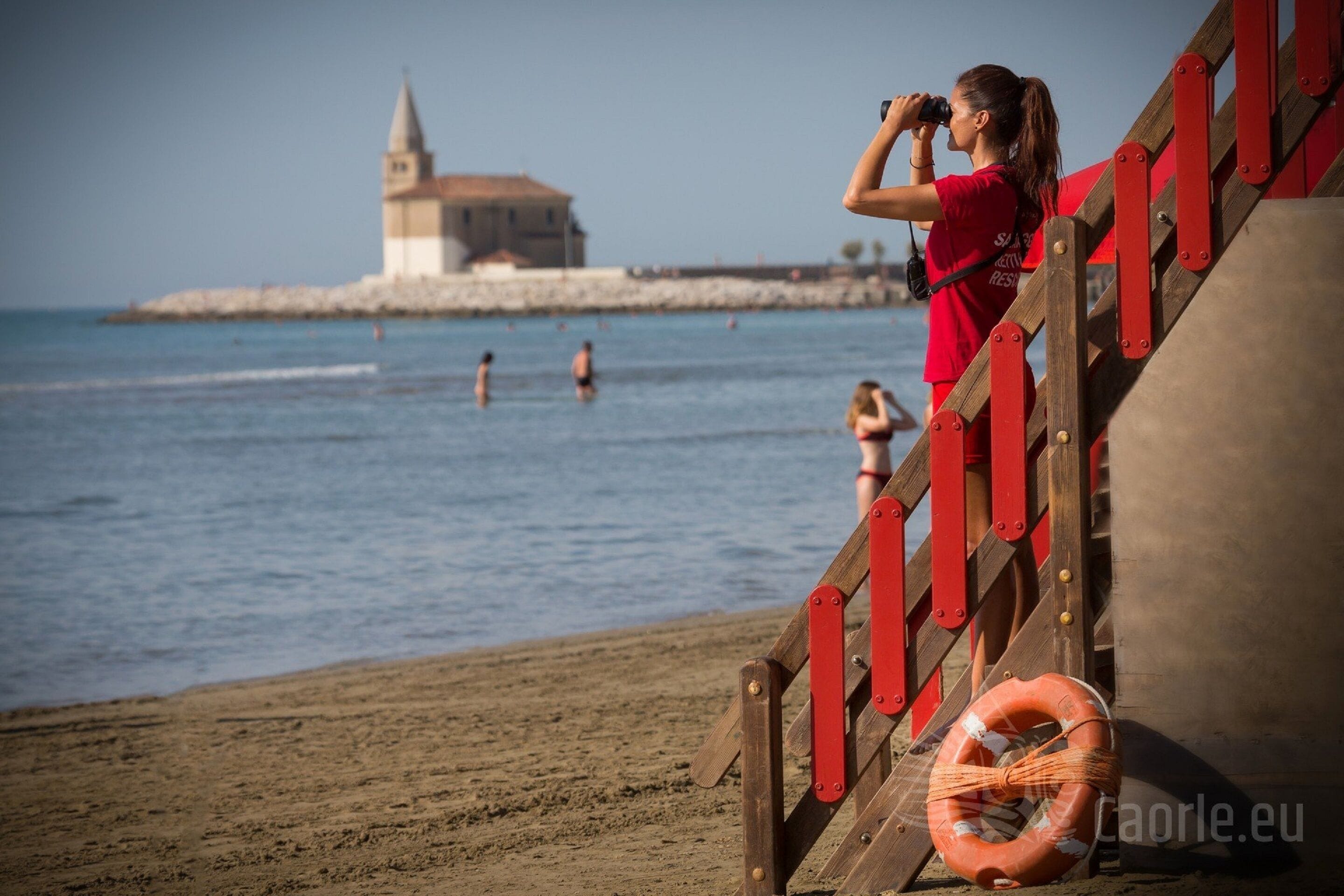 A beach scene with a wooden staircase, a lifebuoy, and a distant building.