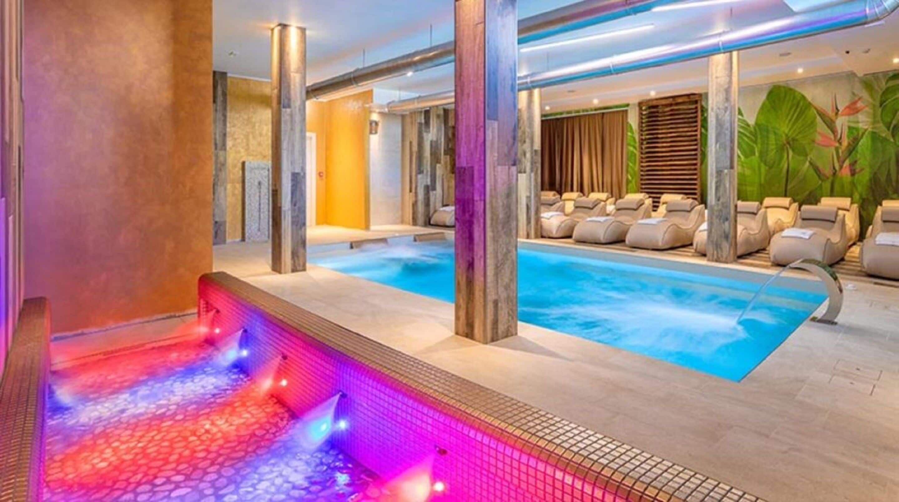 Un área de spa con una bañera de hidromasaje y una piscina, rodeada de sillones de descanso.