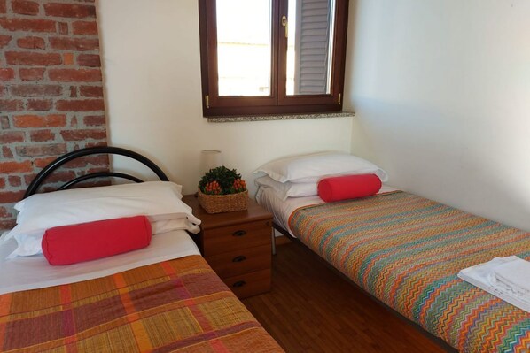 A small, cozy room with two single beds, a wooden dresser, and a window with shutters. - Bnbook-Corte Borromeo 1 (Rho)