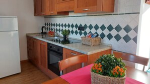 Eine Küche mit Holzausstattung, einem weißen Kühlschrank, einer Spüle und einem Herd. Auf der Arbeitsfläche steht ein Korbkorb mit Blumen.