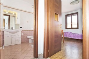 A bathroom with a white sink, mirror, and toilet, and a bedroom with a bed and window. - Bnbook-Corte Borromeo 1 (Rho)