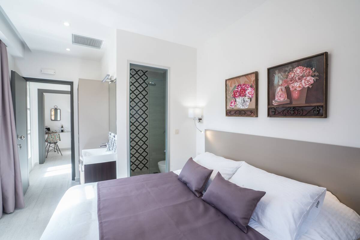 A modern hotel room with a large bed, a bedside table, a mirror, and two paintings on the wall.