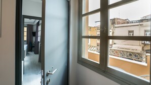 Una habitación con un ventanal grande, una puerta que da a un pasillo y vista a un edificio con un letrero que dice 'Leather art'.