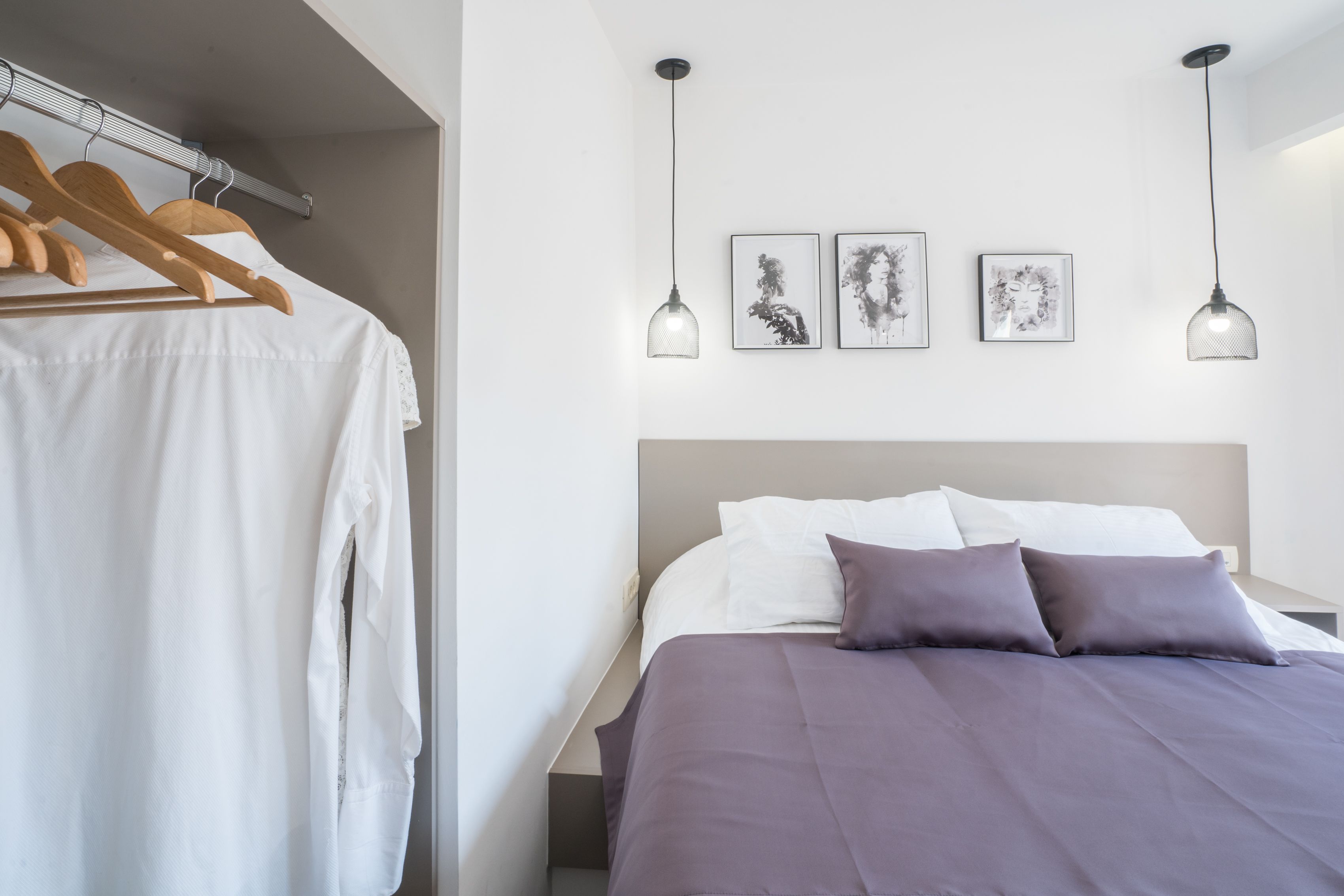 Une chambre avec un lit, un porte-vêtements en bois suspendu et trois lampes suspendues fixées au mur.