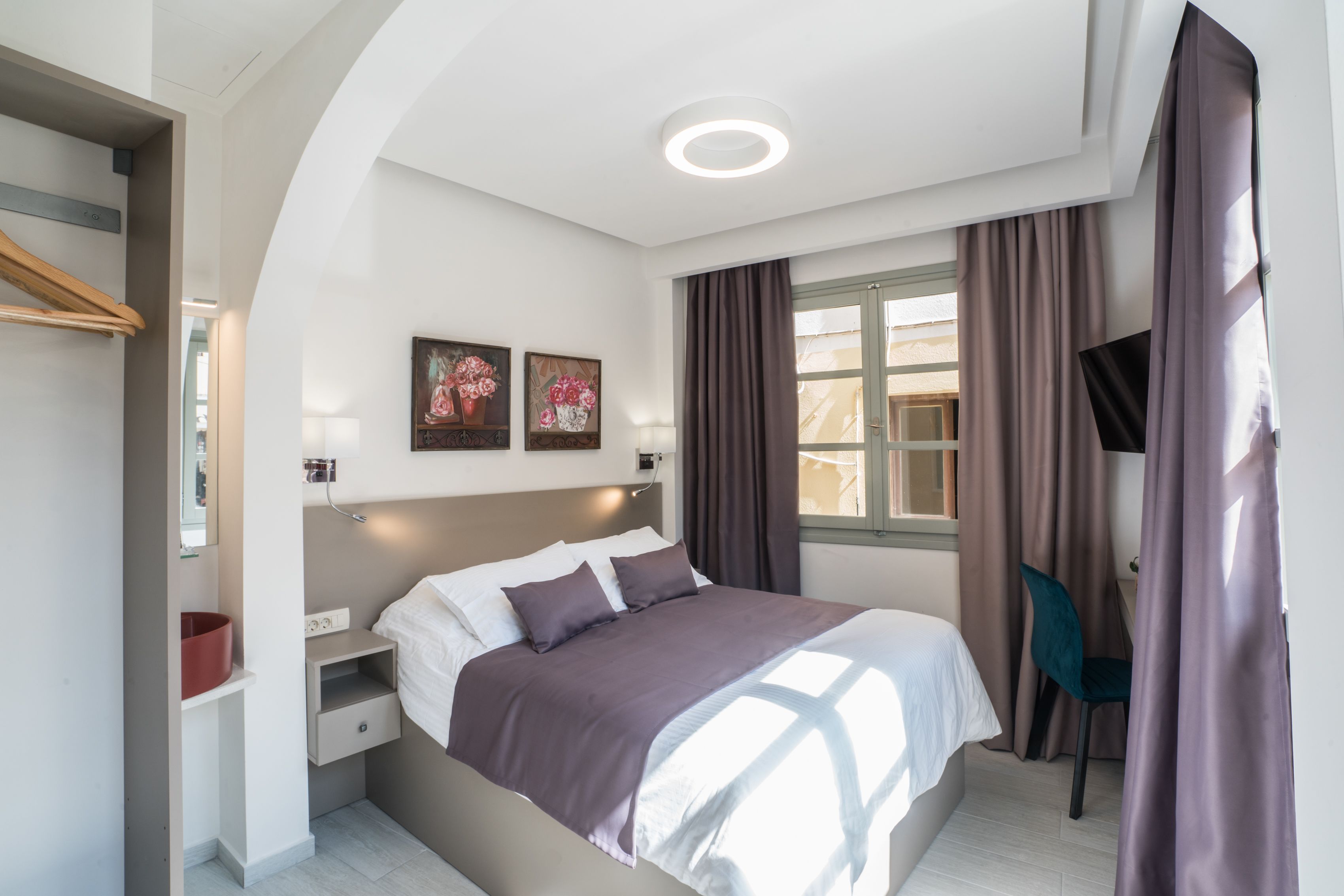 A modern bedroom with a large bed, a bedside table, a chair, and a window with curtains.