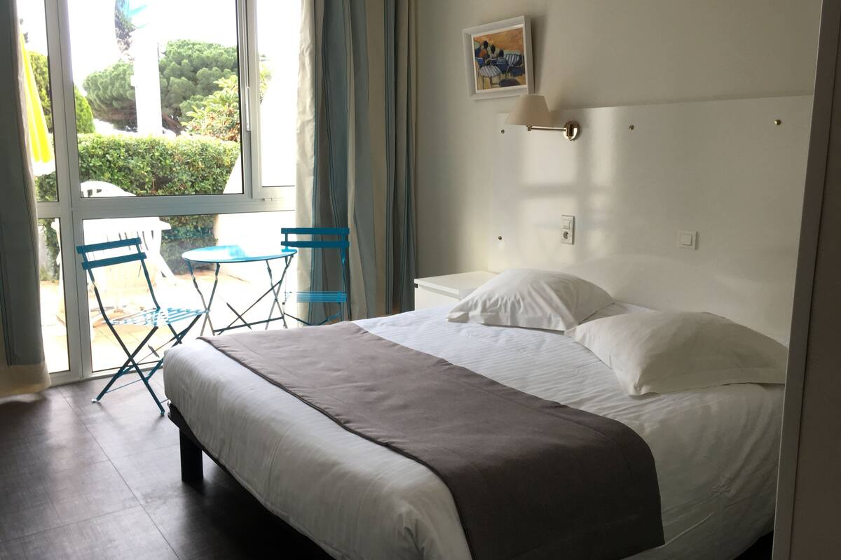 A hotel room with a bed, a small table, chairs, and a view of the outdoors.