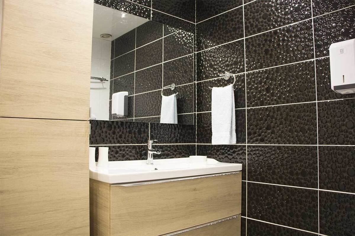A modern bathroom with a white sink, dark patterned tiles, and a mirror reflecting a towel.