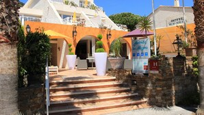Entrada de un hotel con una escalera que lleva al edificio principal, zona de estar al aire libre y un letrero que indica los servicios del hotel.