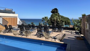 Zona de piscina con sillones de descanso y vista al océano.