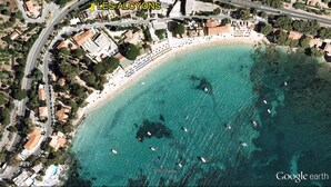Vista aérea de una zona costera con playa, aguas turquesas cristalinas y varios barcos.