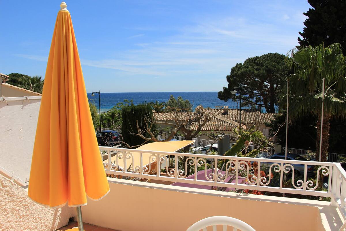 A balcony with a yellow umbrella, a view of the sea, and a white railing.