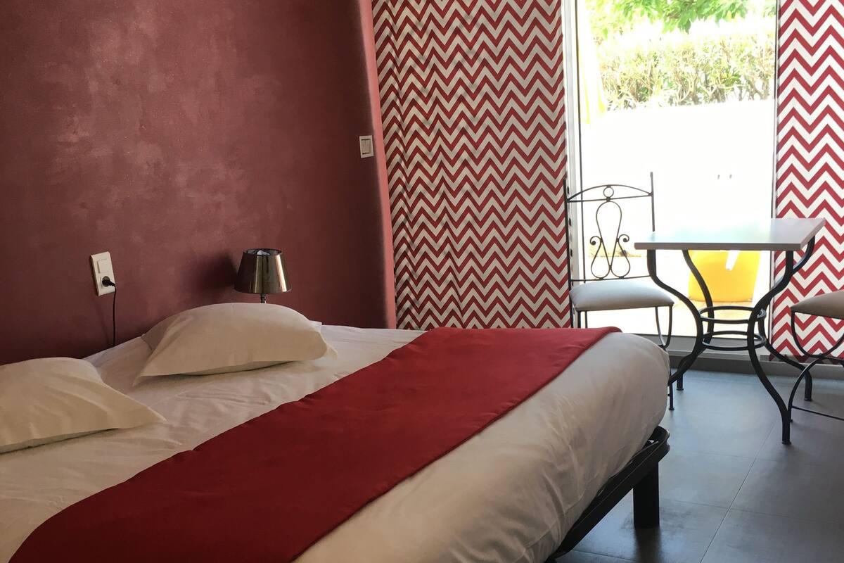 A hotel room with a bed, a lamp, a table, and chairs near a window with chevron-patterned curtains.
