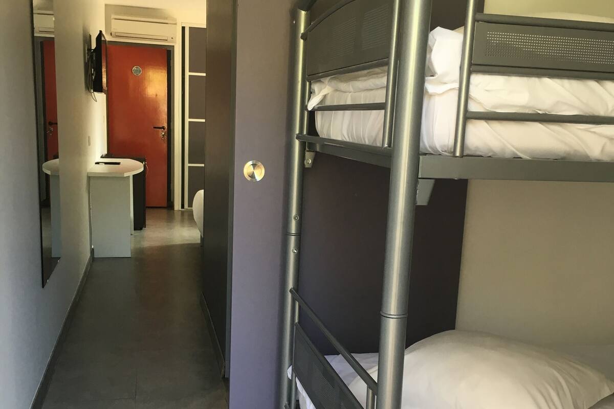 A bunk bed room with a mirror, a small table, and a door leading to a bathroom.