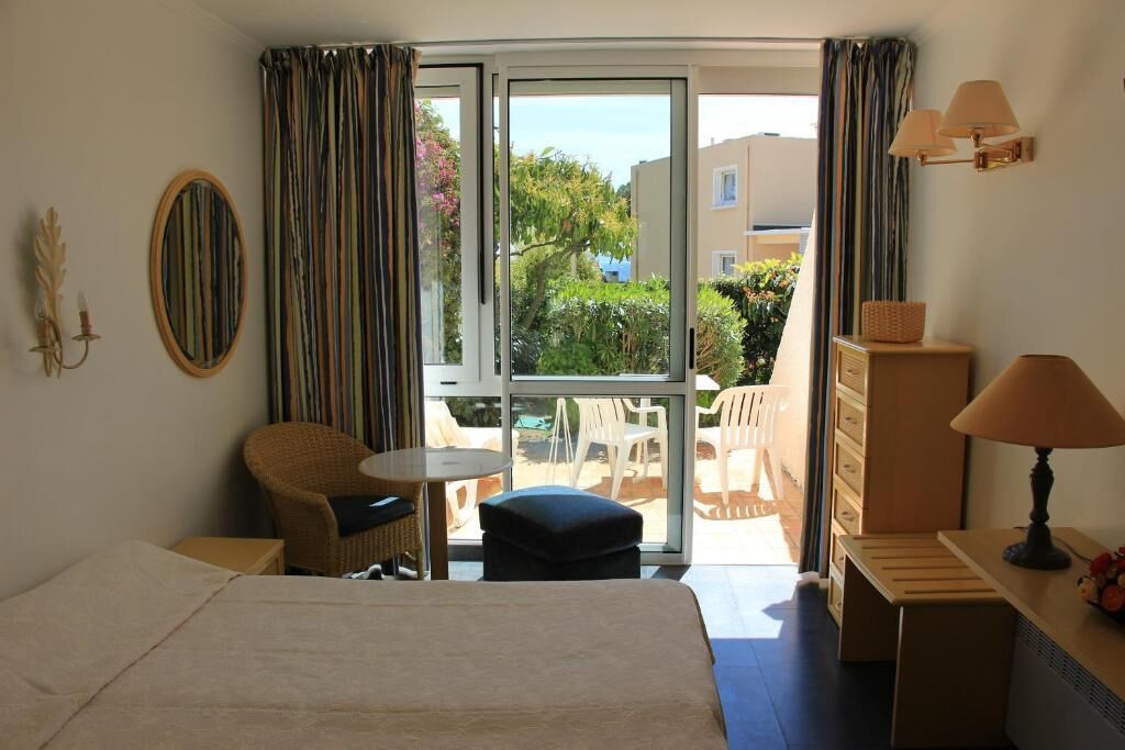 Habitación de hotel con cama, una mesita, una silla, un sofá, una lámpara y vistas al balcón exterior.