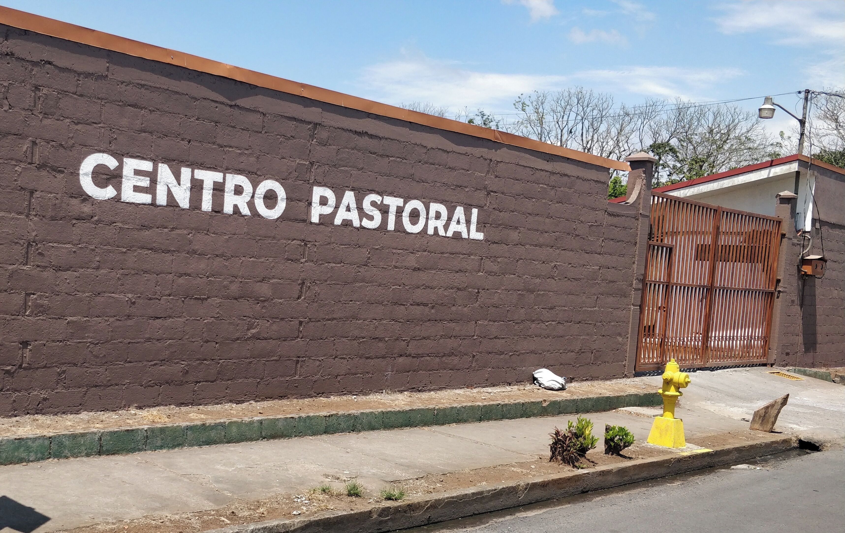 Eine Ziegelwand mit der Aufschrift 'CENTRO PASTORAL', ein eiserner Eingang und ein gelber Feuerlöscher.