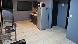 A compact kitchen with a refrigerator, a sink, and a countertop. There is a dining area with a table and chairs. The room has a tiled floor and a wooden ceiling. - Apart. Valhalla San Ramon (San Ramón)