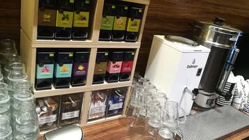Una estación de café con una máquina de café, varios tipos de cápsulas de café y tazas de vidrio.