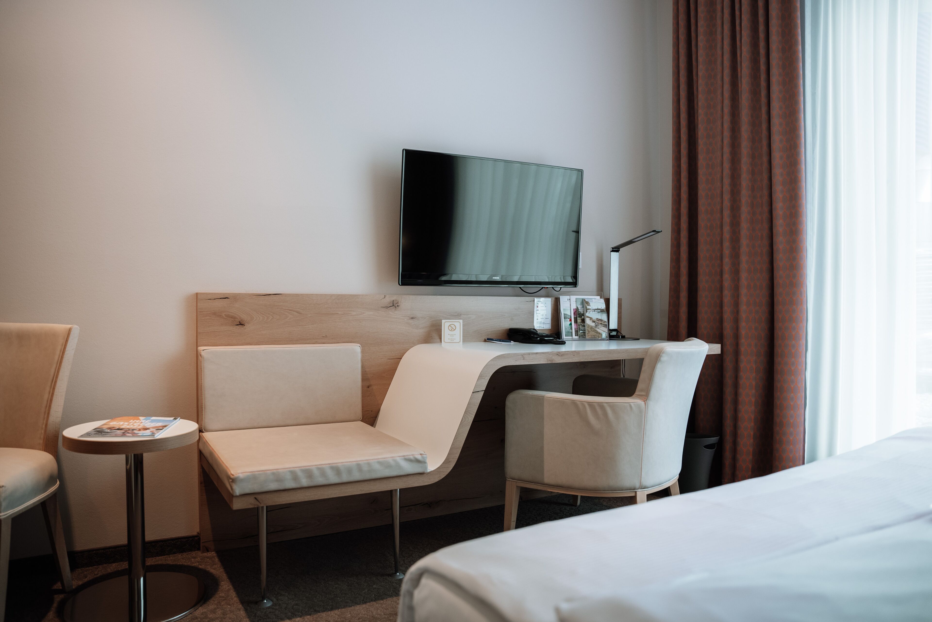 Ein Hotelzimmer mit einem Bett, einem Schreibtisch mit Stuhl, einem Fernseher und einem kleinen Tisch.