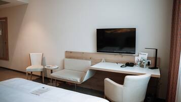 Une chambre d’hôtel comprenant un lit, deux chaises, un bureau, une télévision et une poubelle.