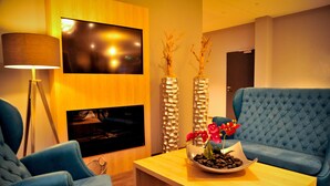 Uma sala de estar moderna com um sofá azul, uma mesa de centro de madeira com um arranjo floral, um abajur e uma TV de tela plana fixada na parede.