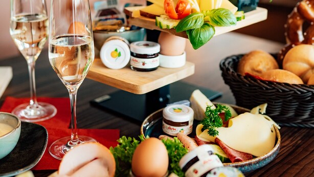 Uma tábua de frutas e queijos em vários níveis, com copos de vinho, uma cesta de pão e diversos acompanhamentos.