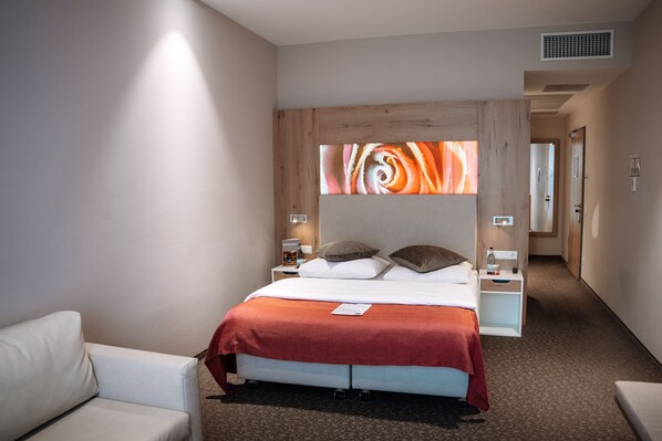 Habitación de hotel moderna con una cama grande, una mesita de noche, una silla y una obra de arte colgada en la pared.