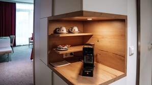 Uma kitchenette compacta com uma máquina de café, uma prateleira pequena com chávenas e uma tigela de petiscos.
