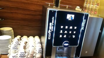 A coffee machine with a digital interface, stacked cups, and plates on a wooden counter.