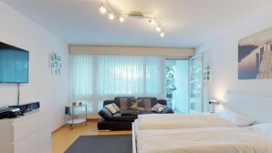 Ein modernes Hotelzimmer mit Bett, einer Couch, einem Fernseher und einem Schreibtisch mit Computer.