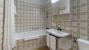Ein Badezimmer mit einer Badewanne, einem Waschbecken und einer Toilette. Die Wände sind mit einem gemusterten Wandpapier versehen, und über dem Waschbecken befindet sich ein Handtuchhalter.