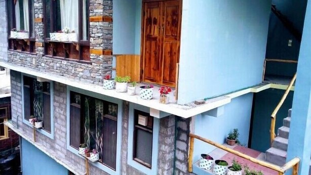 A multi-story building with a stone facade, wooden window frames, and a blue exterior. - Jibhi Cottage (Banjar)