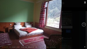 A medium-resolution view of a hotel room with a bed, nightstand, and window with curtains. - Jibhi Cottage (Banjar)