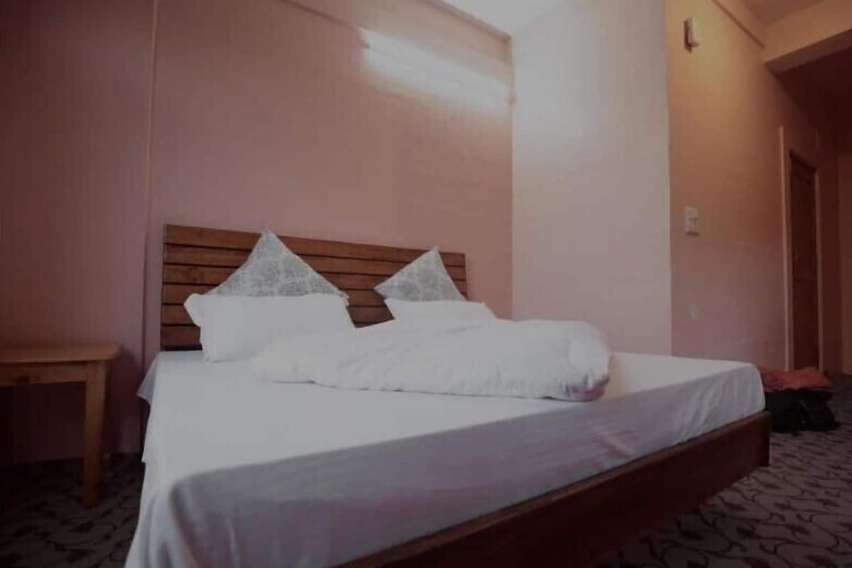 A single bed with a wooden headboard, a bedside table, and a carpeted floor.