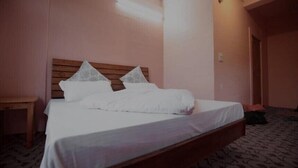 A single bed with a wooden headboard, white bedding, and a patterned carpet. - Jibhi Cottage (Banjar)