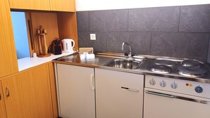 Cocina compacta con lavamanos, estufa y horno, armarios de madera y hervidor.