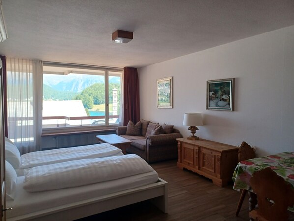 A hotel room with two beds, a sofa, a table, and a view of mountains and a tower. - Super centrally located apartment house in St. Moritz Bad (St. Moritz)