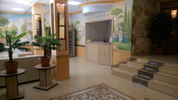 A reception area with a reception desk, a clock, and a staircase leading to an upper floor. - Home Hotel Astana (Astana)