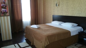 A hotel room with a bed, a nightstand, a lamp, a window with curtains, and a wall with a floral painting. - Home Hotel Astana (Astana)