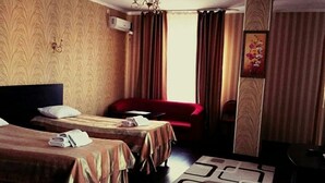 A hotel room with two beds, a red sofa, a chandelier, and a large window with curtains. - Home Hotel Astana (Astana)
