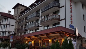Un hotel a più piani con balconi, una zona relax all'aperto coperta e un cartello che indica la presenza di una spa.