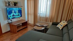 Un soggiorno con un divano, un tavolino, una TV e un piccolo tavolo con una pianta.