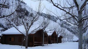 Una hilera de cabañas de madera con tejados nevados, rodeadas de árboles desnudados y un suelo cubierto de nieve.