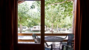 Una terraza de madera con una mesa y sillas, con vista a un estacionamiento donde se observan vehículos recreativos y árboles.