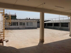 A spacious covered area with a concrete floor, a metal staircase, and a building with a tiled roof in the background. - Hotel Royal Residency (Pakur)