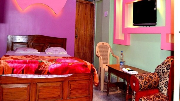 A bedroom with a bed, a TV mounted on the wall, and a chair. - Hotel Royal Residency (Pakur)