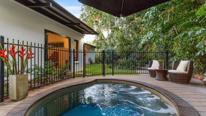 Ein Pool mit Backsteinbordierung, umgeben von einem schwarzen Metallzaun und einer Terrasse mit Korbmöbeln.